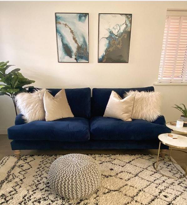 Blue sofa with fluffy cushions and art work hanging on the wall above it
